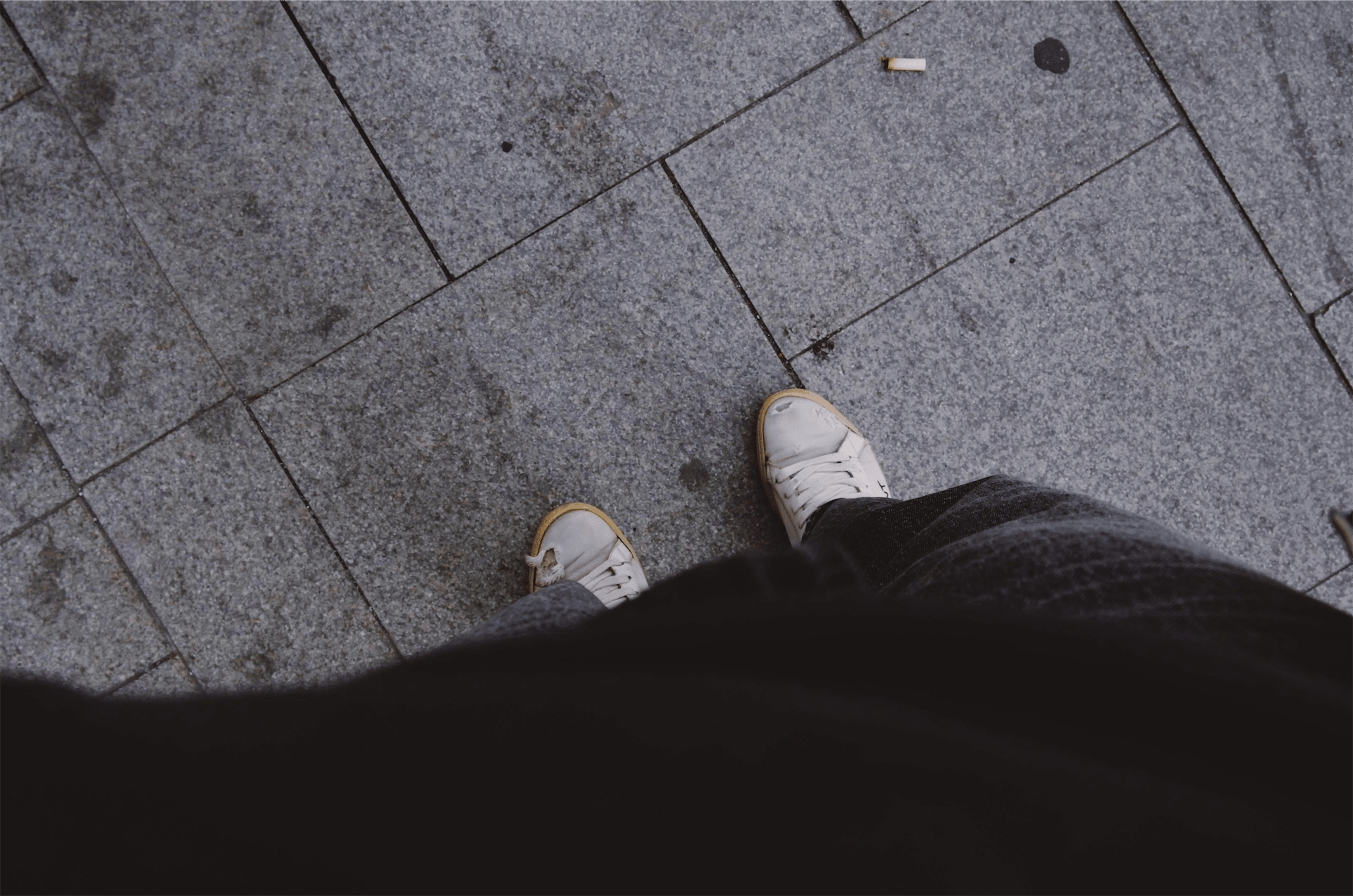 a cigarette butt on the ground in front of a smoker's shoes